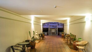 Un pasillo con mesas y sillas, una estatua y vista de un edificio al fondo.