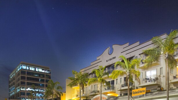 Un hotel con varios balcones, palmeras y un cartel que dice "Raine&Horne".