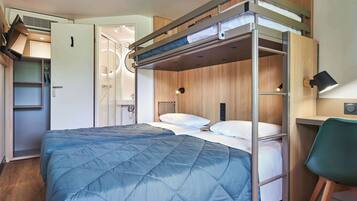 A bunk bed with a blue quilt, a desk with a chair, and a wardrobe.