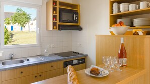 A modern kitchen with a built-in microwave, a dishwasher, and a window with a view of a tree and buildings. - Résidence Lagrange Vacances Les Jardins Renaissance (Azay-le-Rideau)