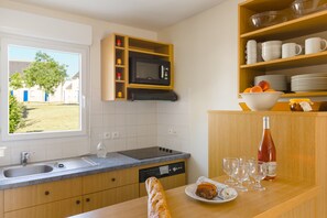 A modern kitchen with a built-in microwave, a dishwasher, and a window with a view of a tree and buildings. - Résidence Lagrange Vacances Les Jardins Renaissance (Azay-le-Rideau)