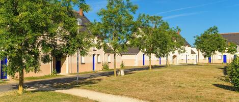A row of buildings with blue doors, surrounded by trees and a clear sky.