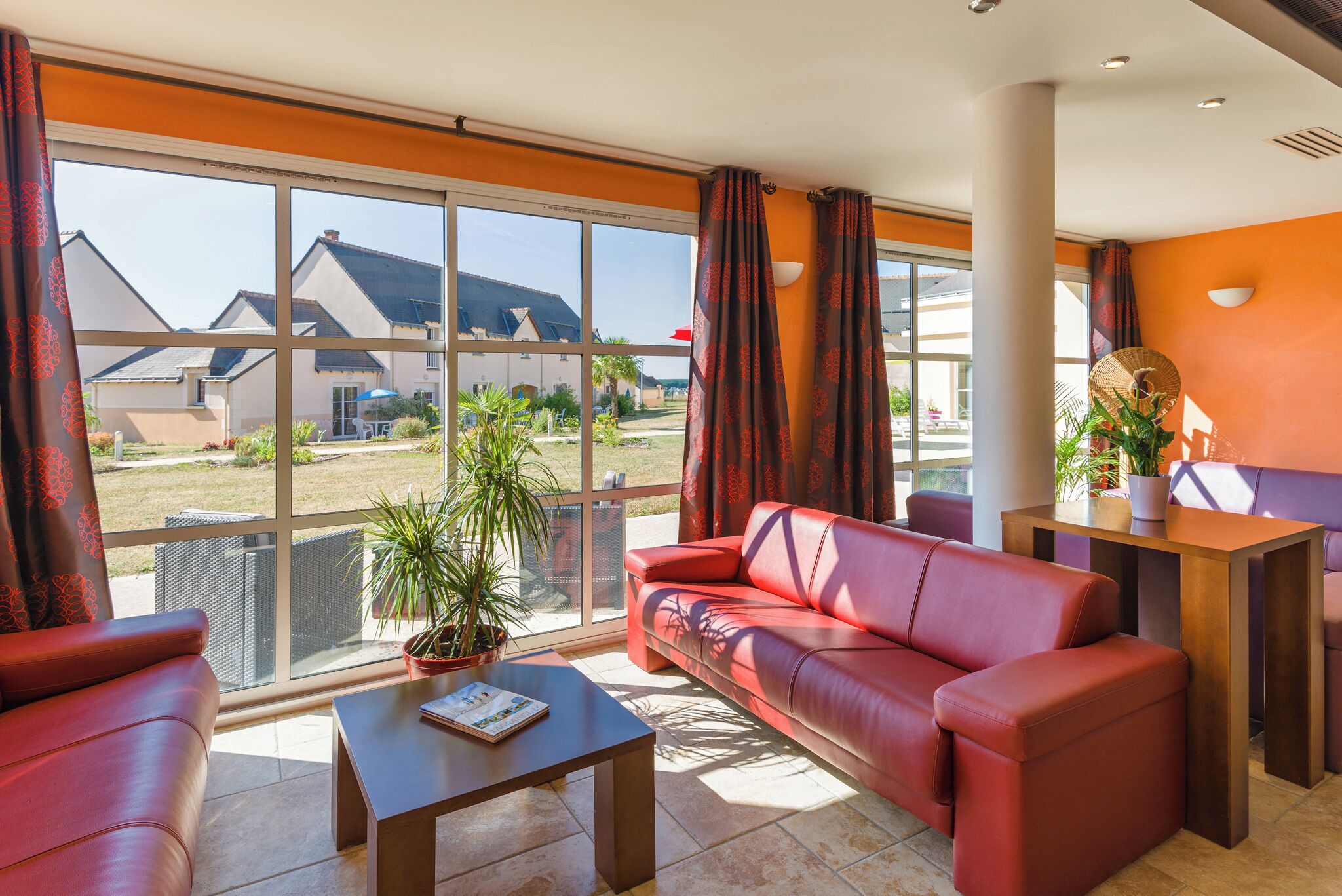 A modern living room with a red sofa, a coffee table, and a large window offering a view of houses.