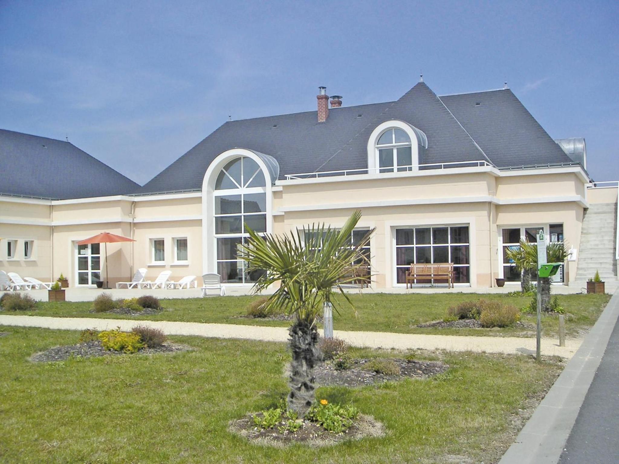 A two-story house with a large front lawn, a palm tree, and a bench.