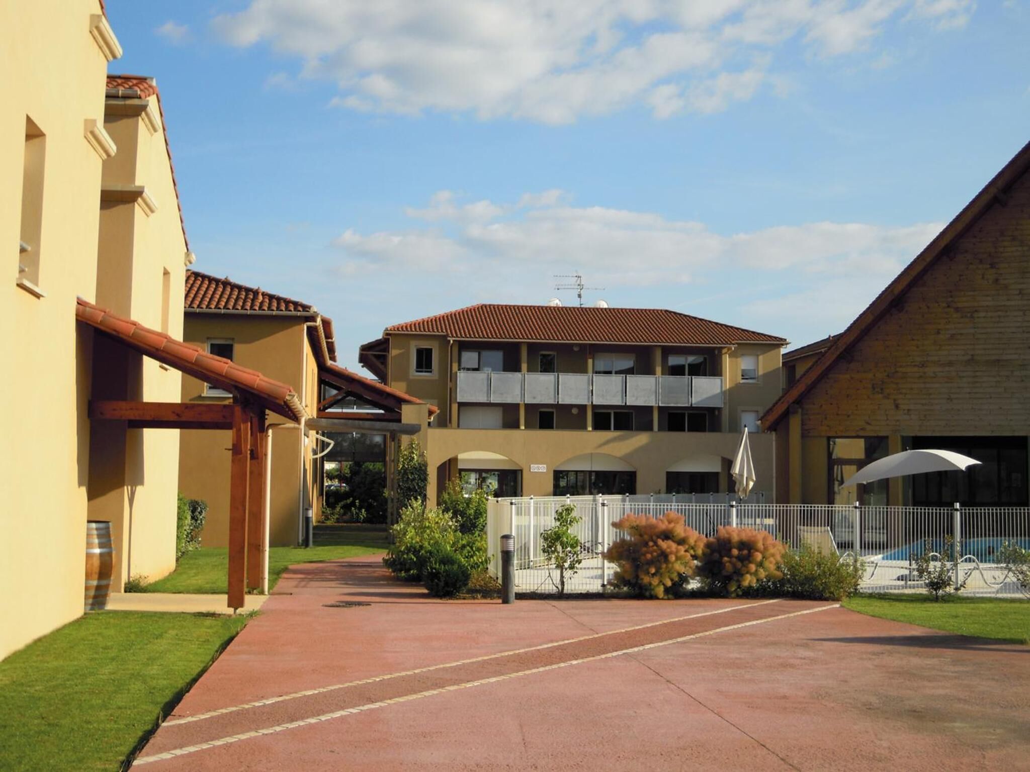 Ein Innenhof mit einem Gebäude, das ein rotes Ziegeldach, einen überdachten Gang und einen eingezäunten Bereich mit einem Pool hat.