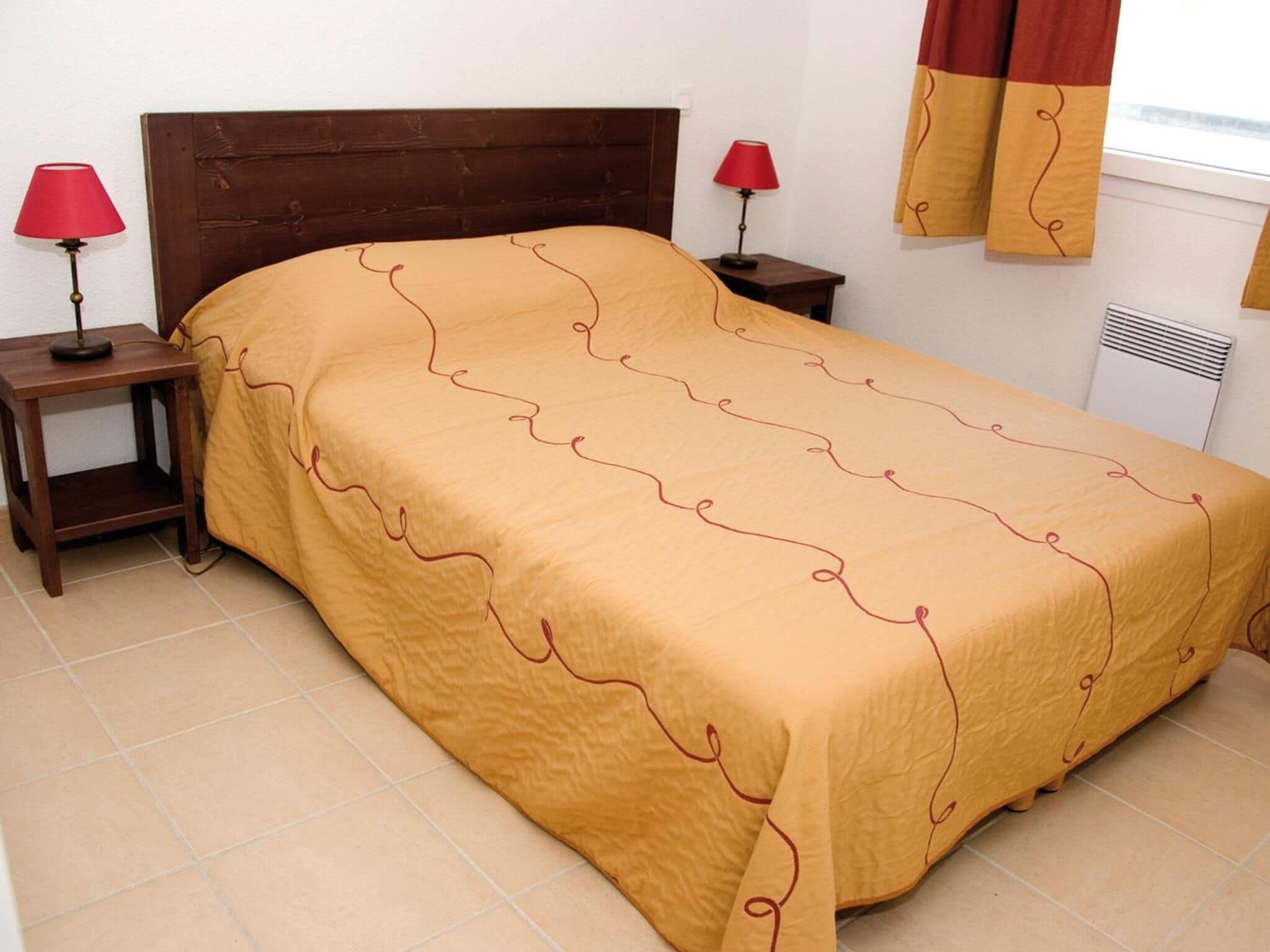 A single bed with a brown headboard, two bedside tables with lamps, and a window with curtains.
