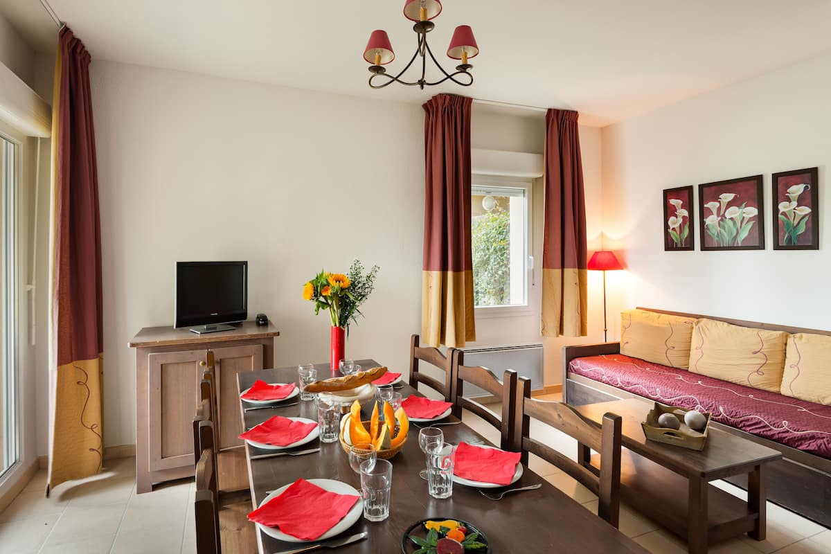 A dining area with a table set for two, a television, and a sofa.