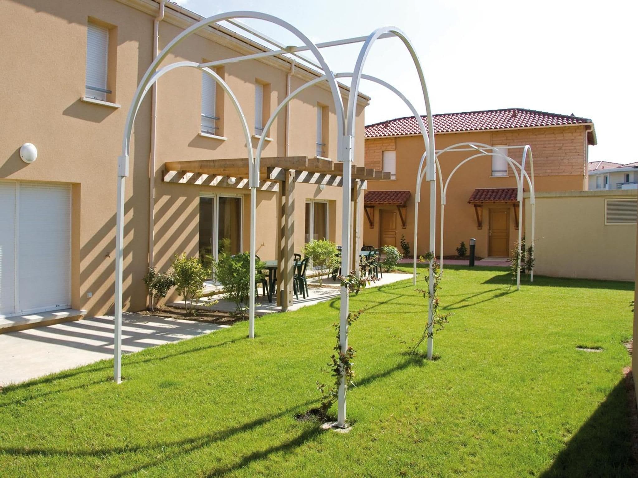 A courtyard with a pergola, a small seating area, and a building with a tiled roof.