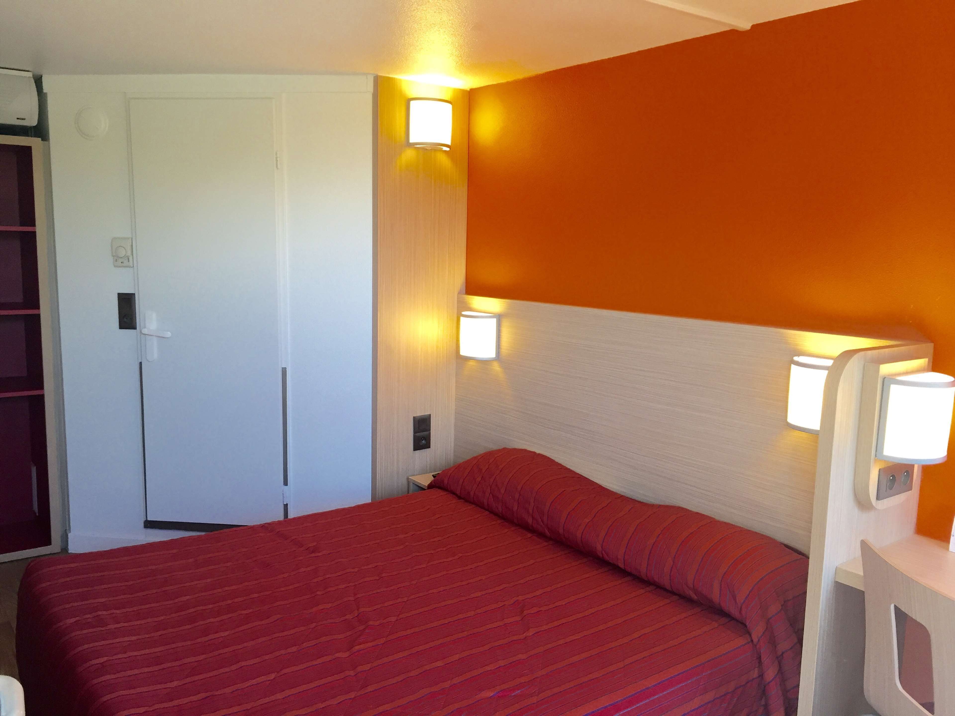 A hotel room with a bed, a door, and two wall-mounted lights.