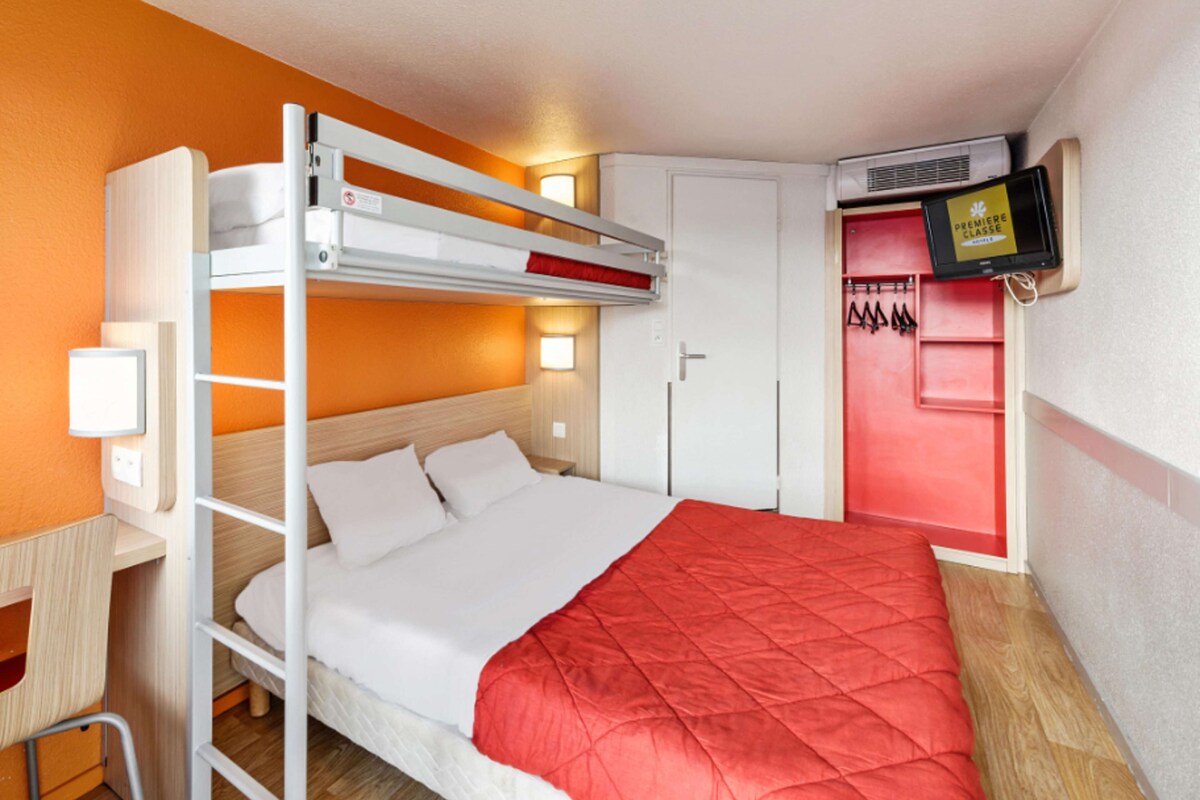 A bunk bed room with a desk, a TV, and a wardrobe.