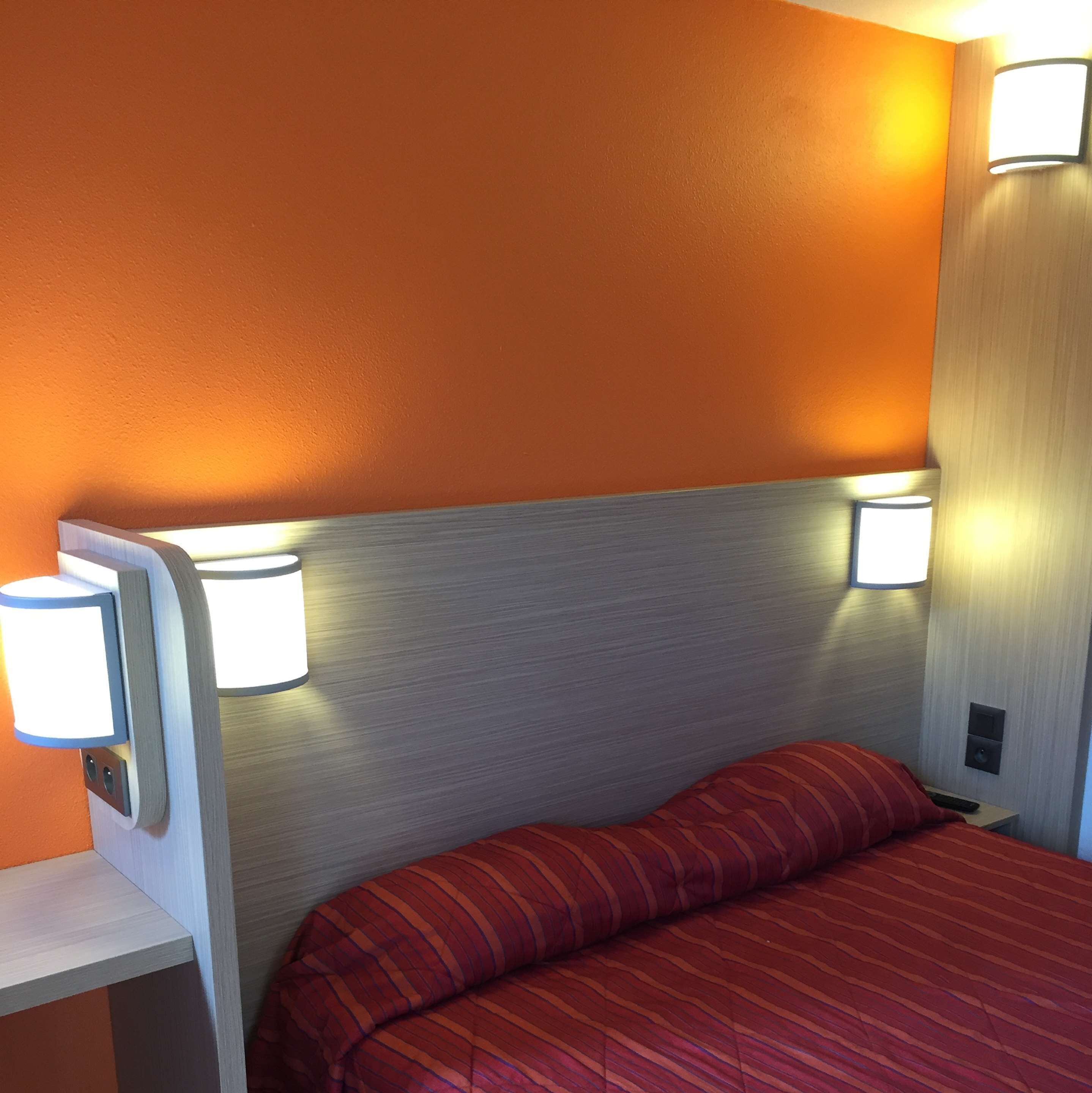 A hotel room with a bed, two wall-mounted lamps, and a nightstand.