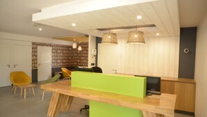 A modern reception area with a wooden reception desk, a green accent, and a bookshelf in the background. - Premiere Classe SETE - Balaruc (Balaruc-le-Vieux)