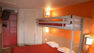 A bunk bed with a red quilted bedspread, a white door, a small bedside table with a lamp, and a wall-mounted TV.