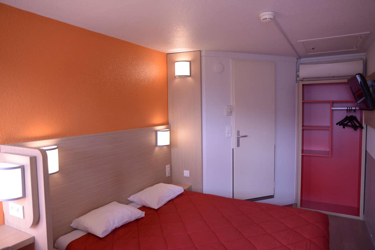 A hotel room with a bed, a wardrobe, and a TV mounted on the wall.