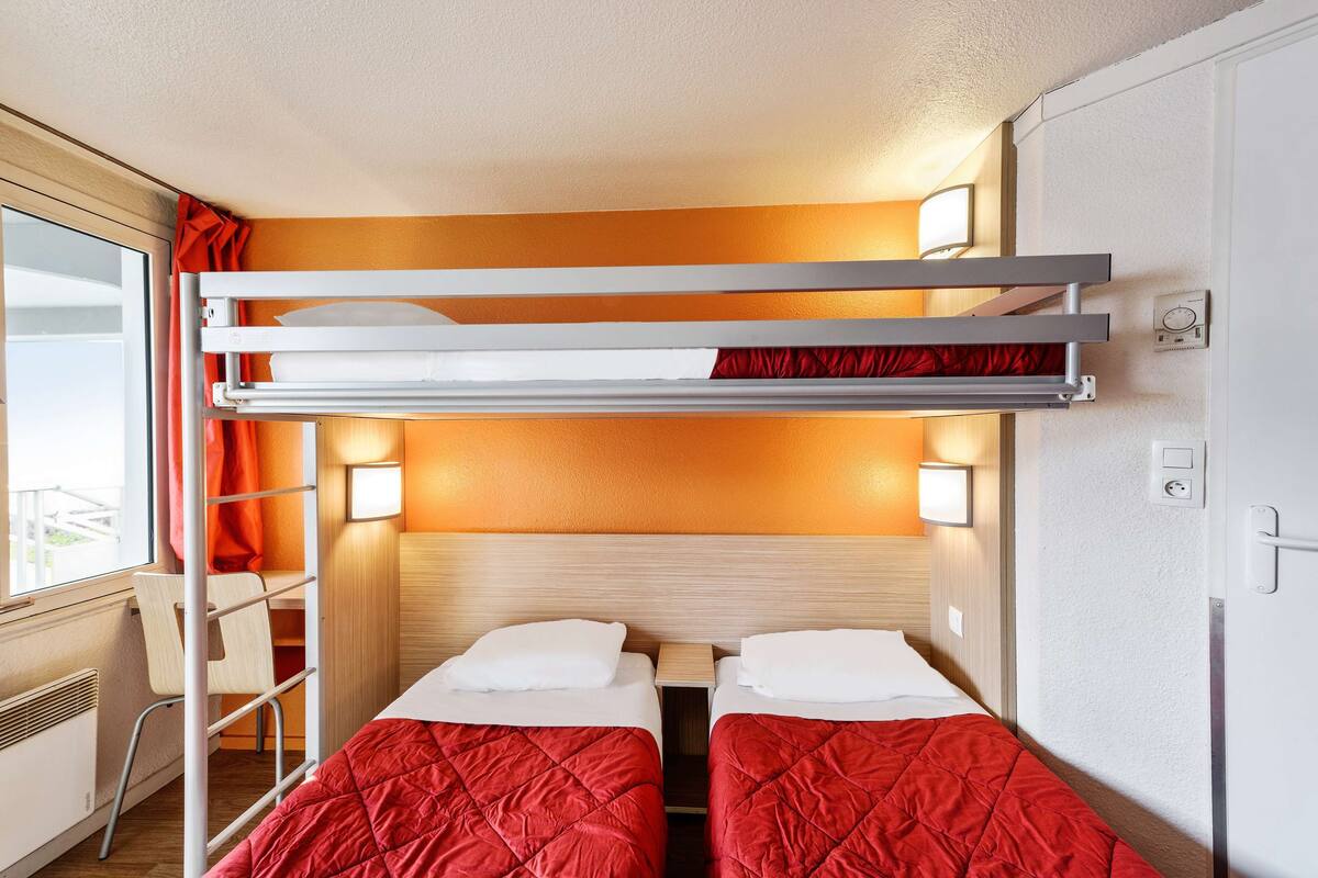A compact room with bunk beds, a desk, and a window with curtains.