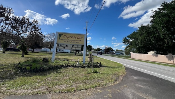 A sign for Cypress Inn advertising amenities like efficiencies, mobile homes, and a jacuzzi room, with a clear sky and a road in the background.