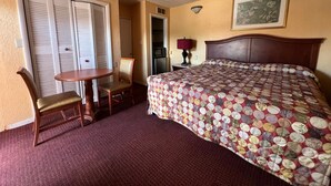 A hotel room with a bed, a chair, a small table, a lamp, and a door with shutters.