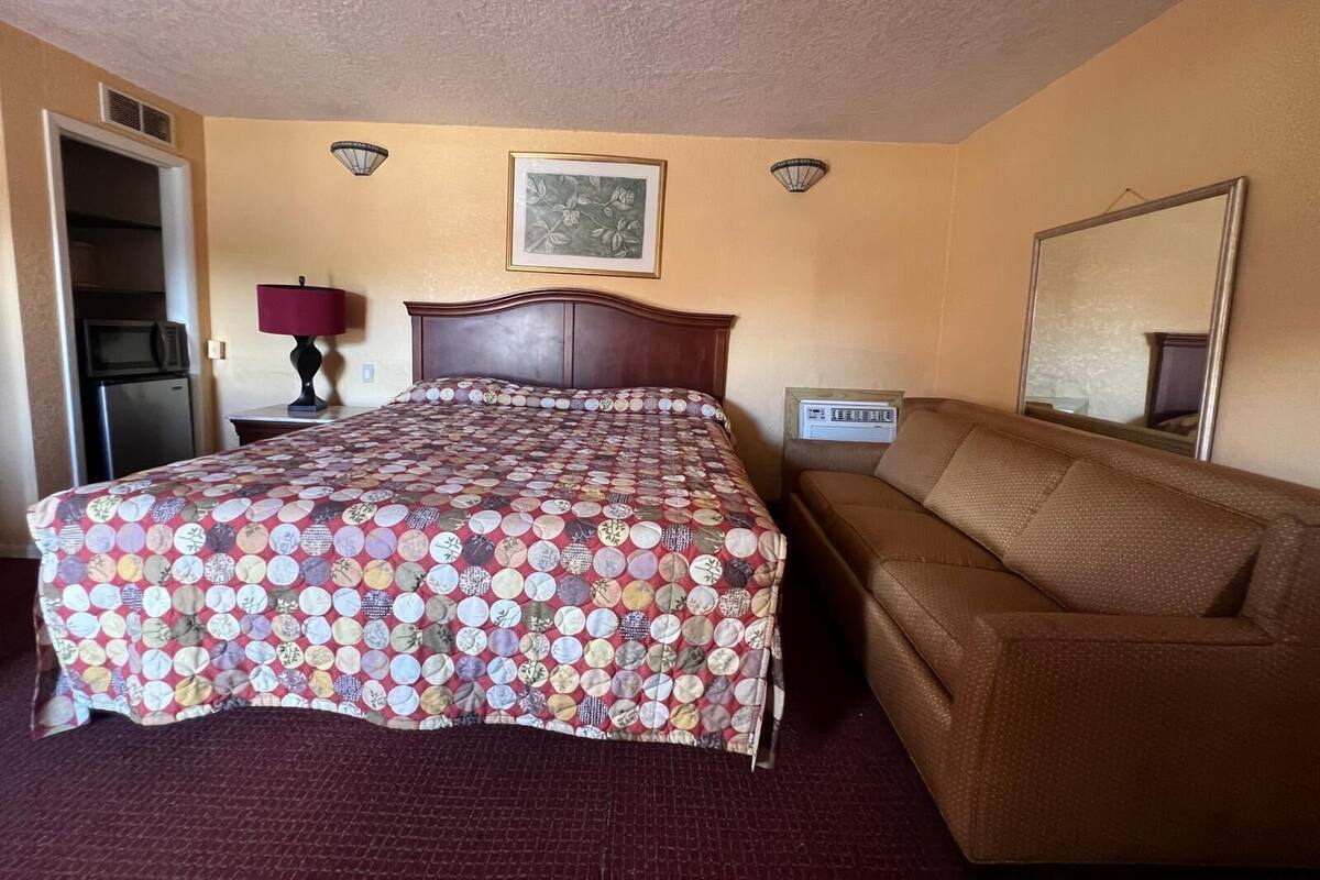 Ein Hotelzimmer mit einem Bett, einer Couch, einem Bild an der Wand, einem Spiegel und einer Küchenzeile.
