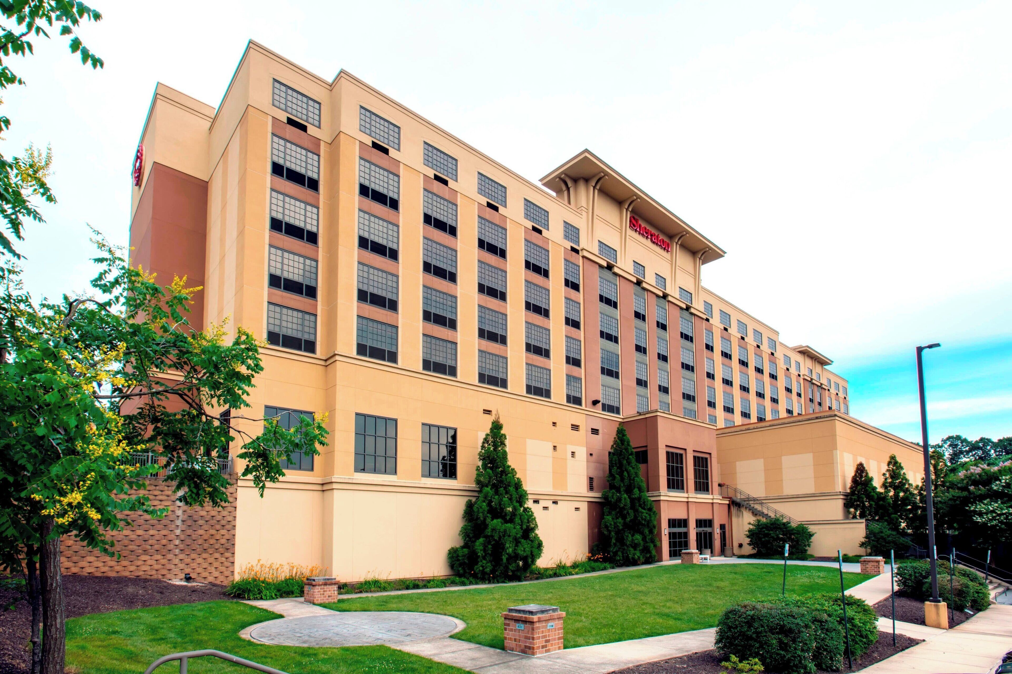 Un hotel grande con varios pisos, una entrada principal y un césped cuidado con árboles y arbustos.