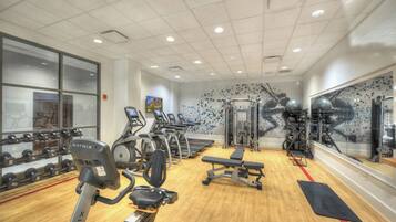 A gym with cardio machines, free weights, and a mirror wall.