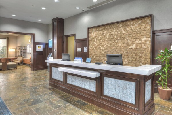 A hotel reception area with a marble counter, wooden paneling, and a potted plant.