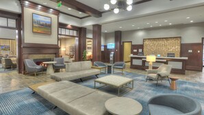 Um hall com sofás, poltronas, uma mesa de centro, uma lareira e um balcão de recepção.