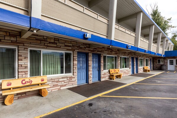 A motel with a row of rooms, each with a blue door and a bench outside.