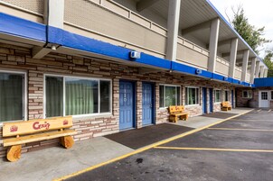 A motel with a row of rooms, each with a blue door and a bench outside.