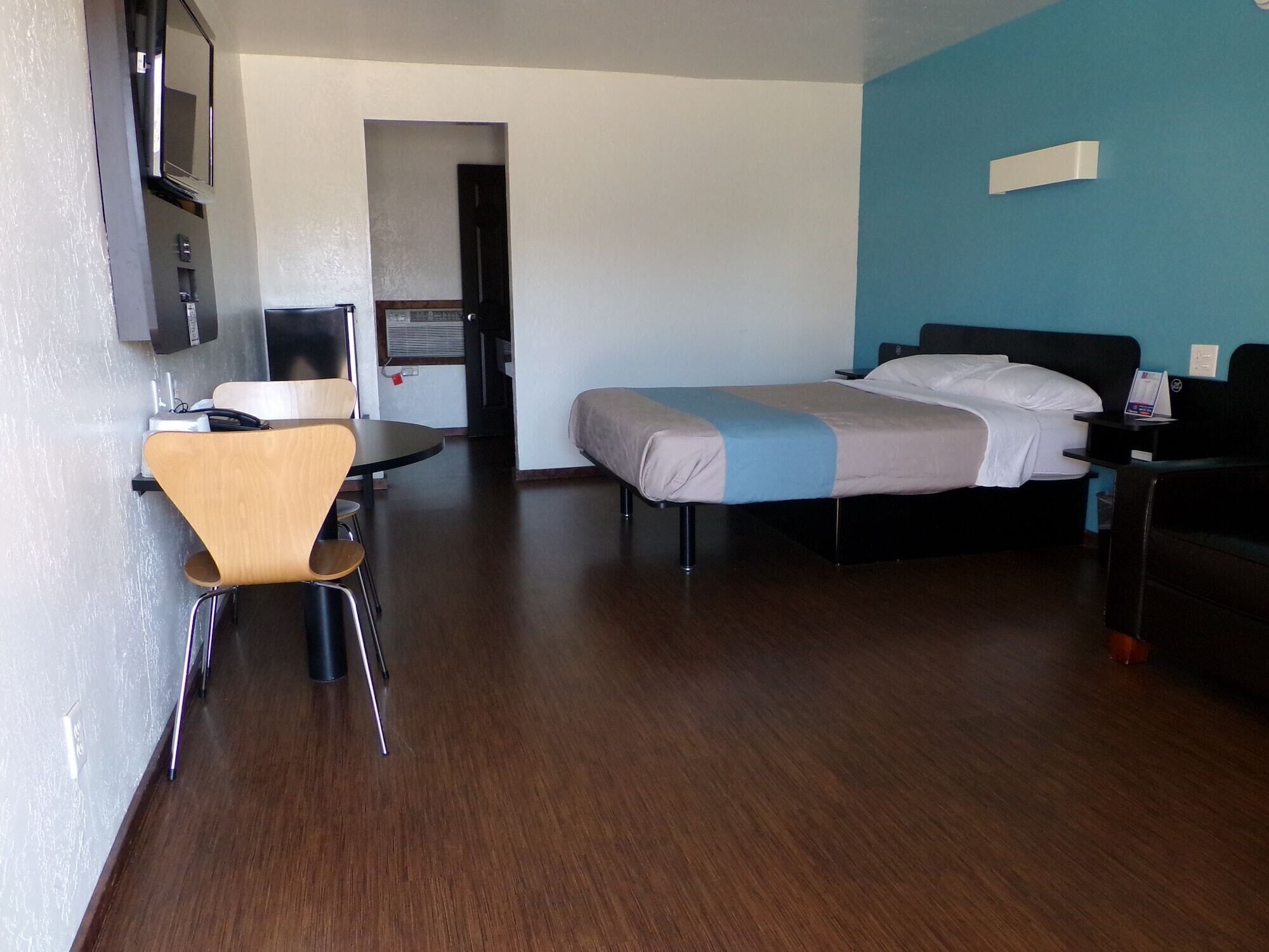 Una habitació d'hotel amb un llit, una taula, una cadira, un televisor i una porta que dona a un bany.