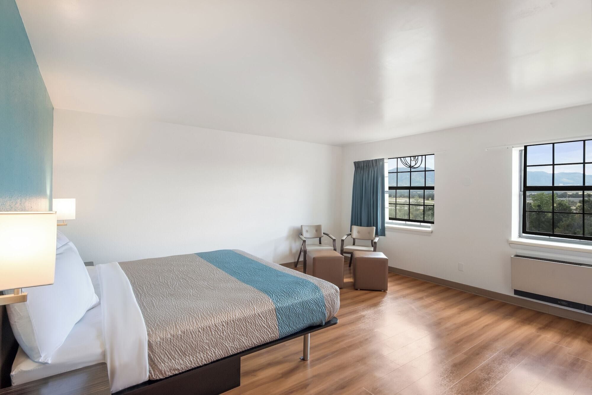 Una habitación de hotel con cama, escritorio, dos sillas, ventana con vistas y una lámpara.