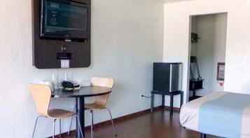 A hotel room with a bed, a desk with two chairs, a television mounted on the wall, and a door leading to another room.