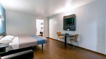 Una habitación de hotel con cama, escritorio, dos sillas, televisor montado en la pared y puerta que da a otra habitación.