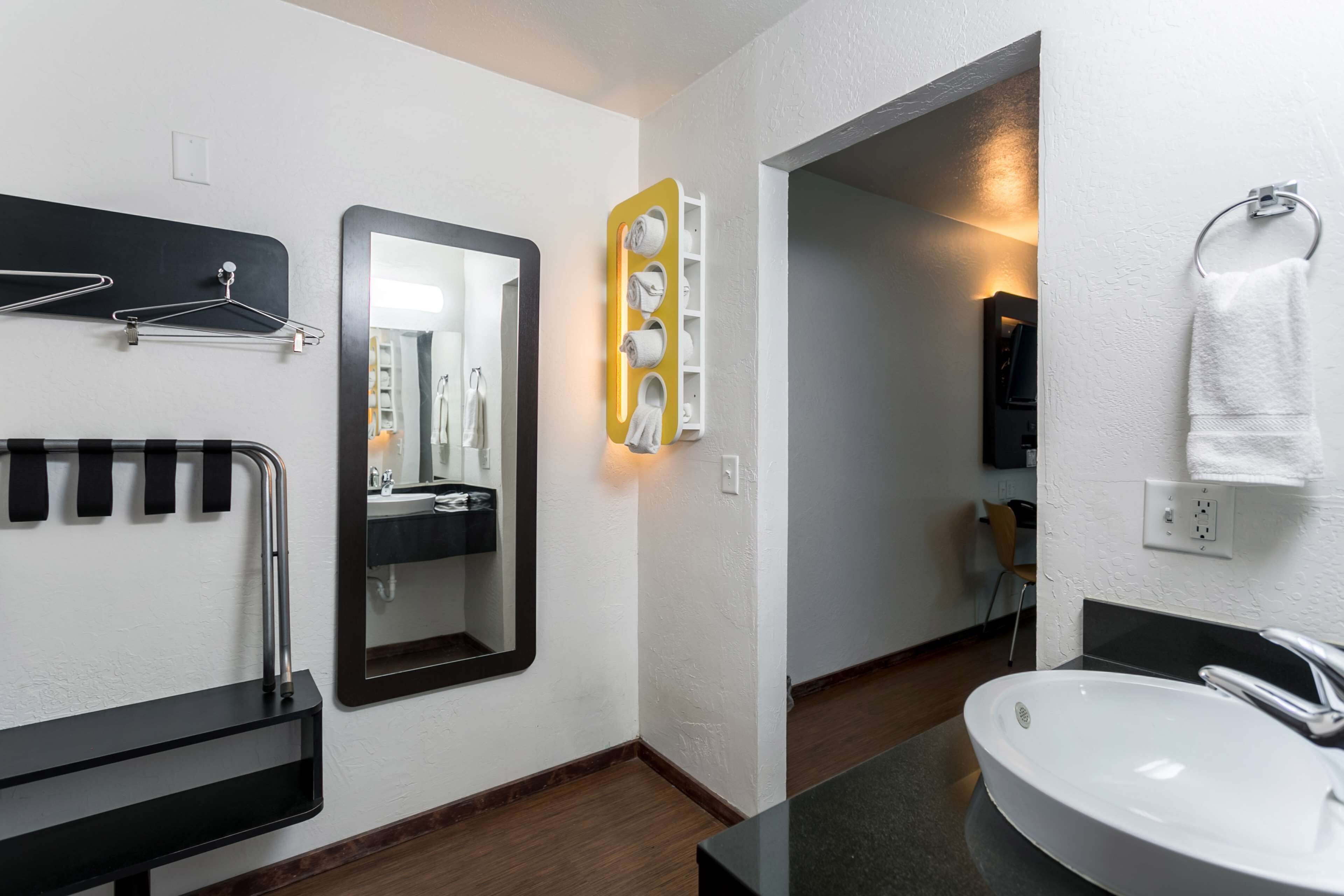 Une salle de bain moderne avec un porte-serviettes noir, un miroir, un lavabo blanc et une serviette suspendue à un anneau.
