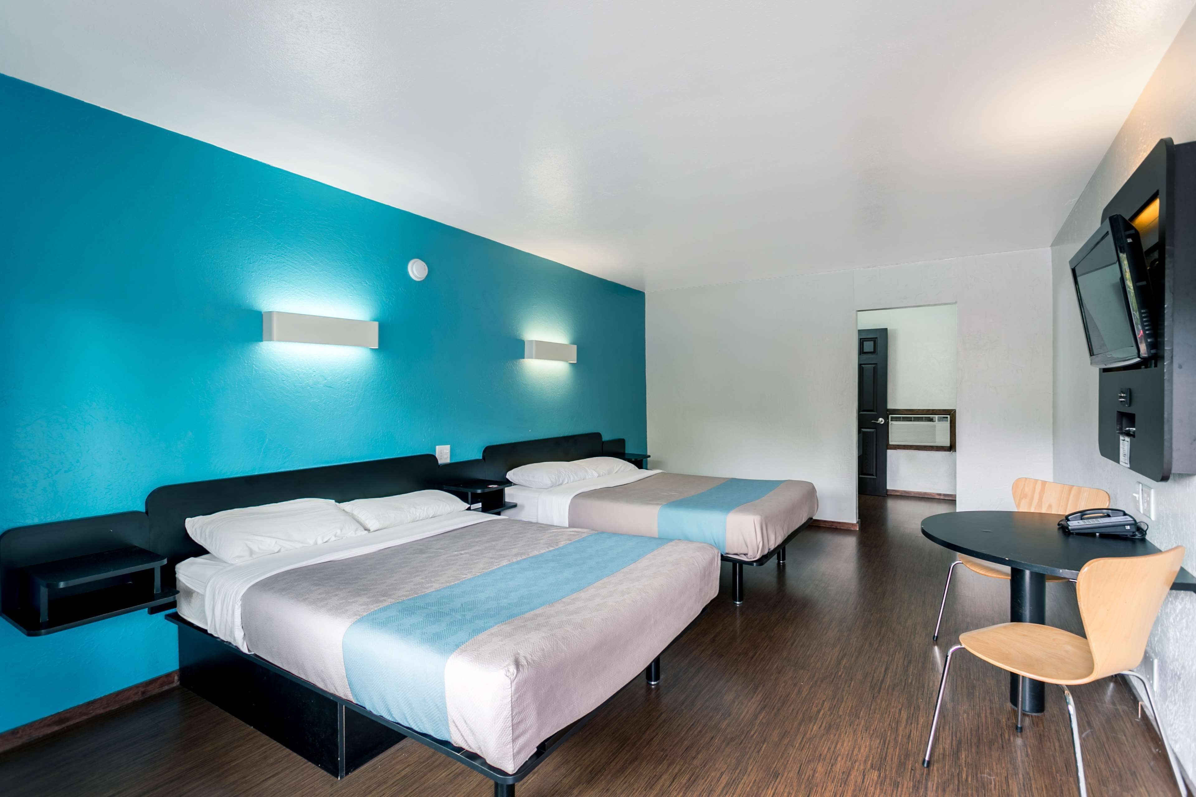 Een hotelkamer met twee bedden, een bureau, een stoel, een televisie en een deur naar een andere kamer.