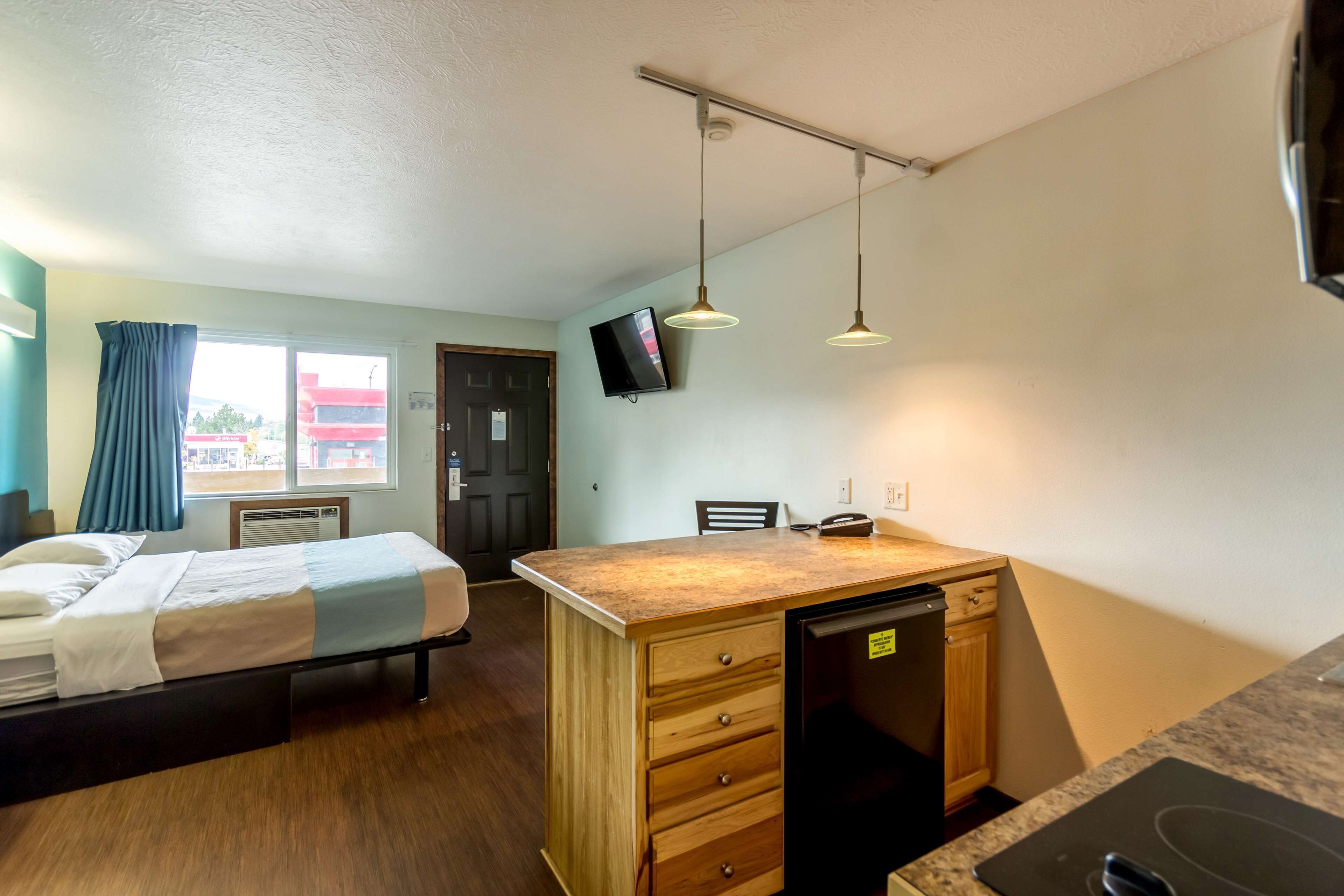 A compact hotel room with a bed, a small desk with a sink, and a television mounted on the wall.