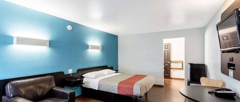A hotel room with a bed, a desk, a chair, a sofa, and a TV.