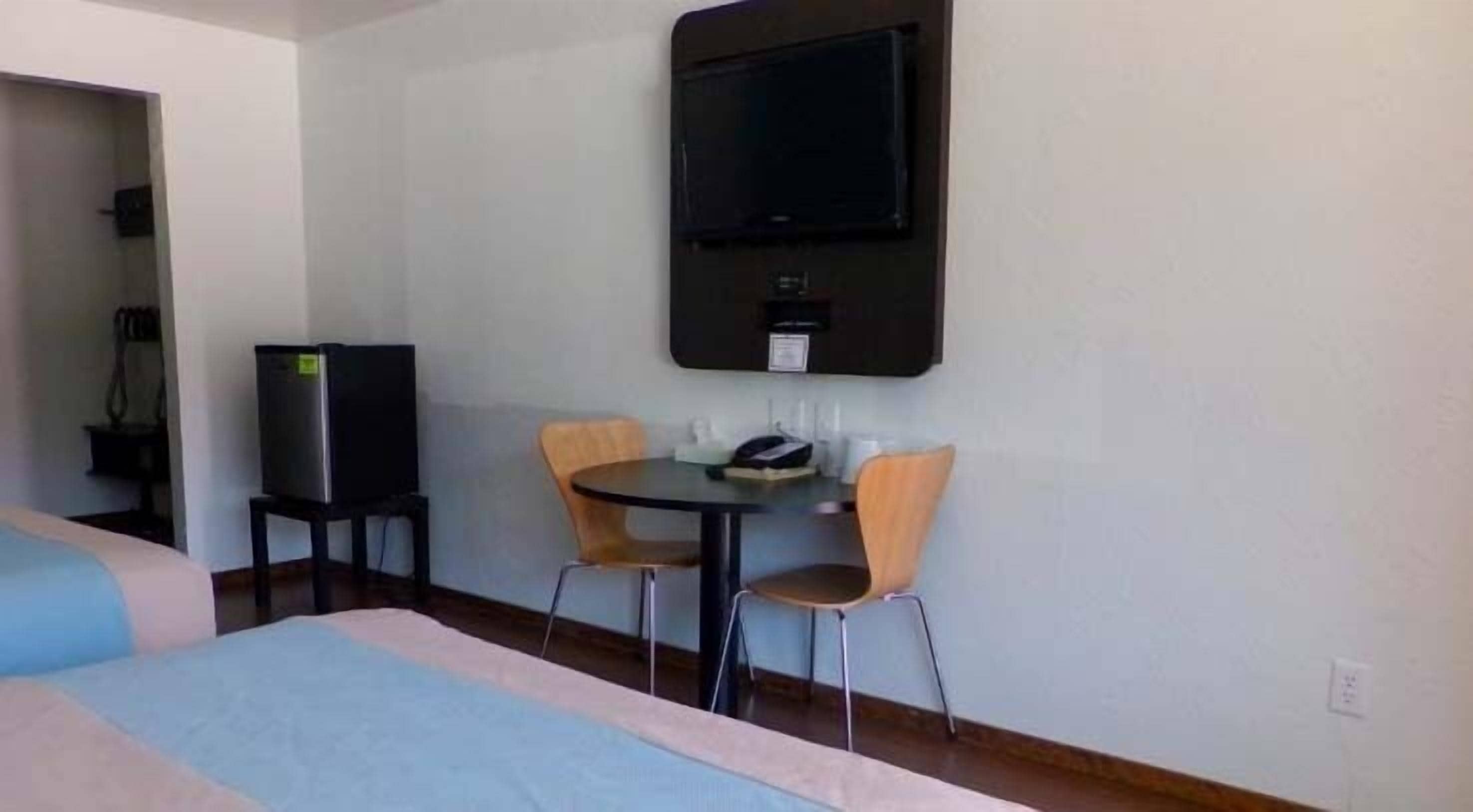 Habitación de hotel con cama, escritorio y dos sillas, televisor montado en la pared y refrigerador.