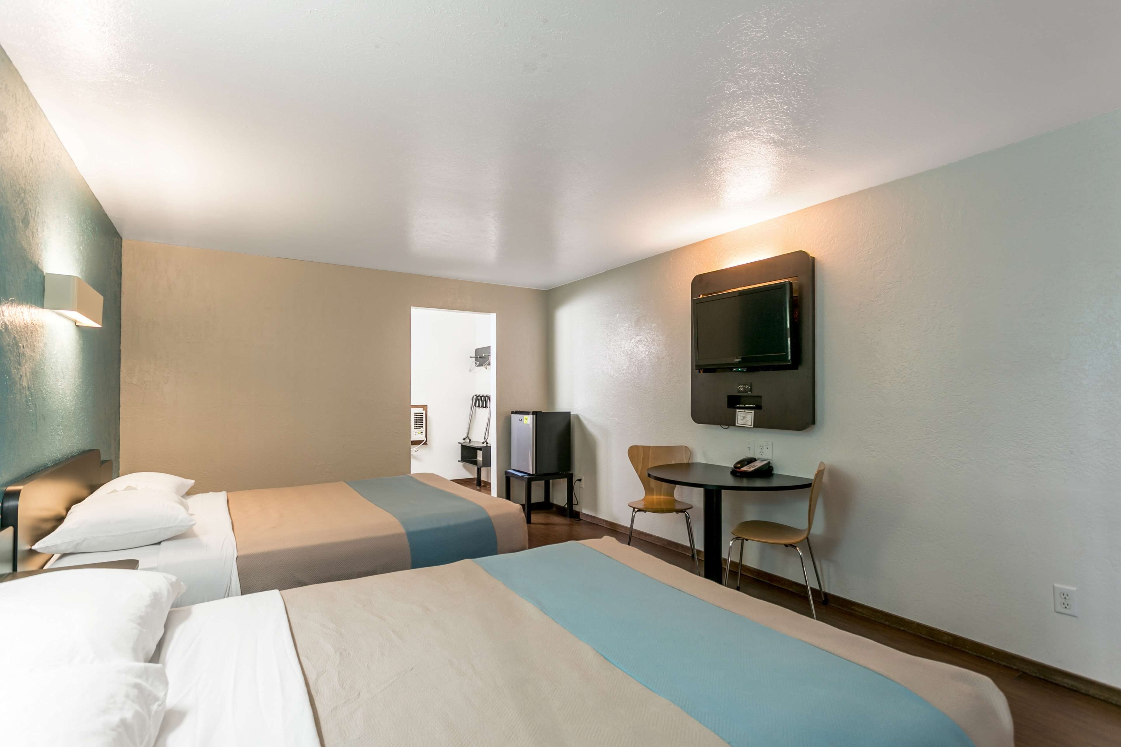 A hotel room with two beds, a desk, a chair, a television, and a small table.