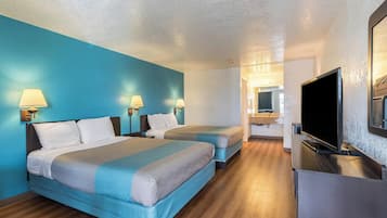 Habitación de hotel con dos camas, un televisor y un baño visible a través de una puerta abierta.