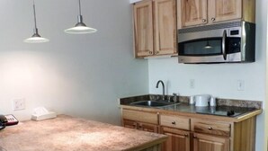 A kitchen with wooden cabinets, a stainless steel microwave, a sink, and two pendant lights. - Motel 6 University Missoula (Missoula)