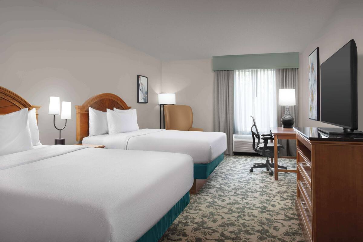 A hotel room with two beds, a desk, a chair, a television, and a window with curtains.