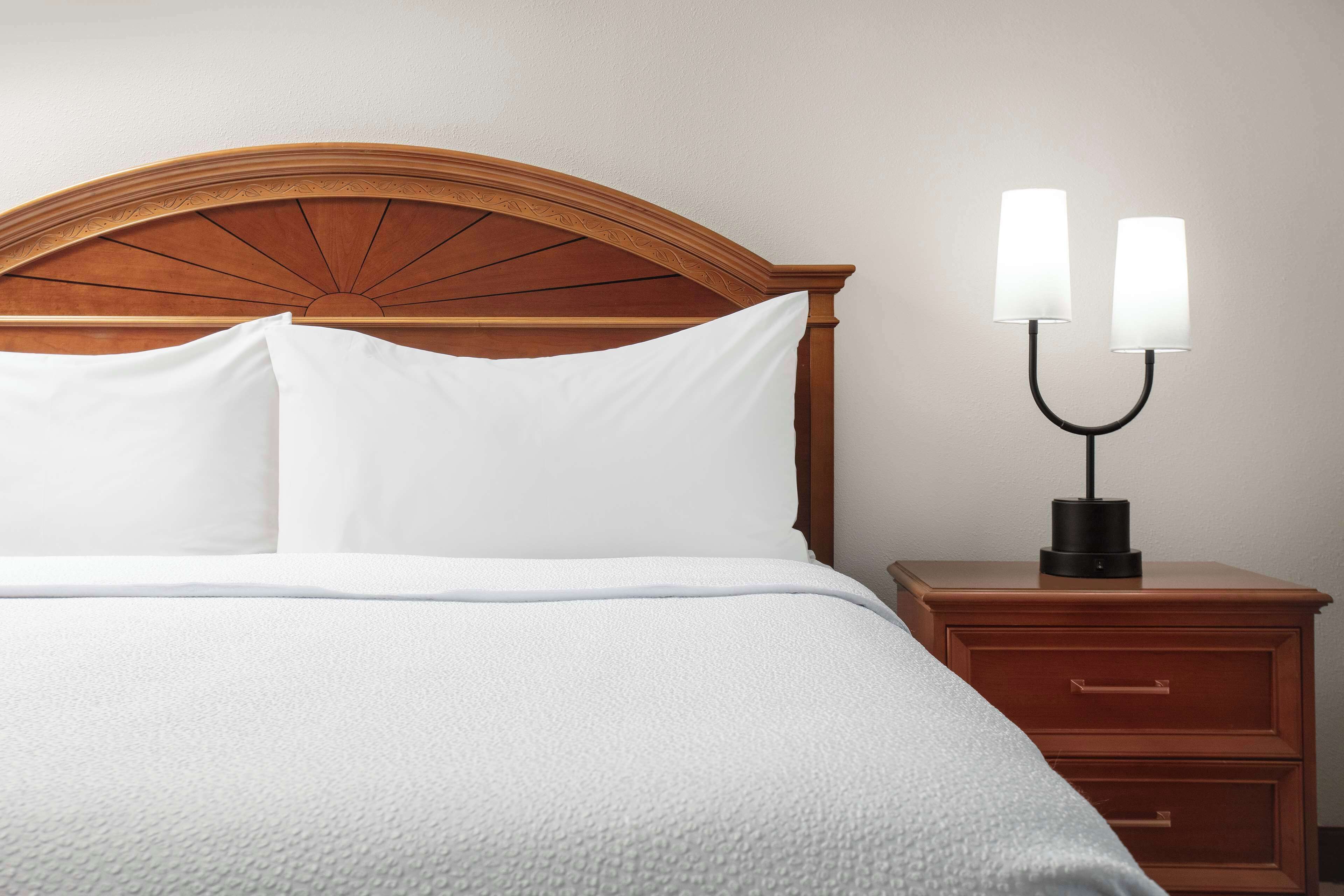 A neatly made bed with white linens, a wooden headboard, and a bedside table with a lamp.