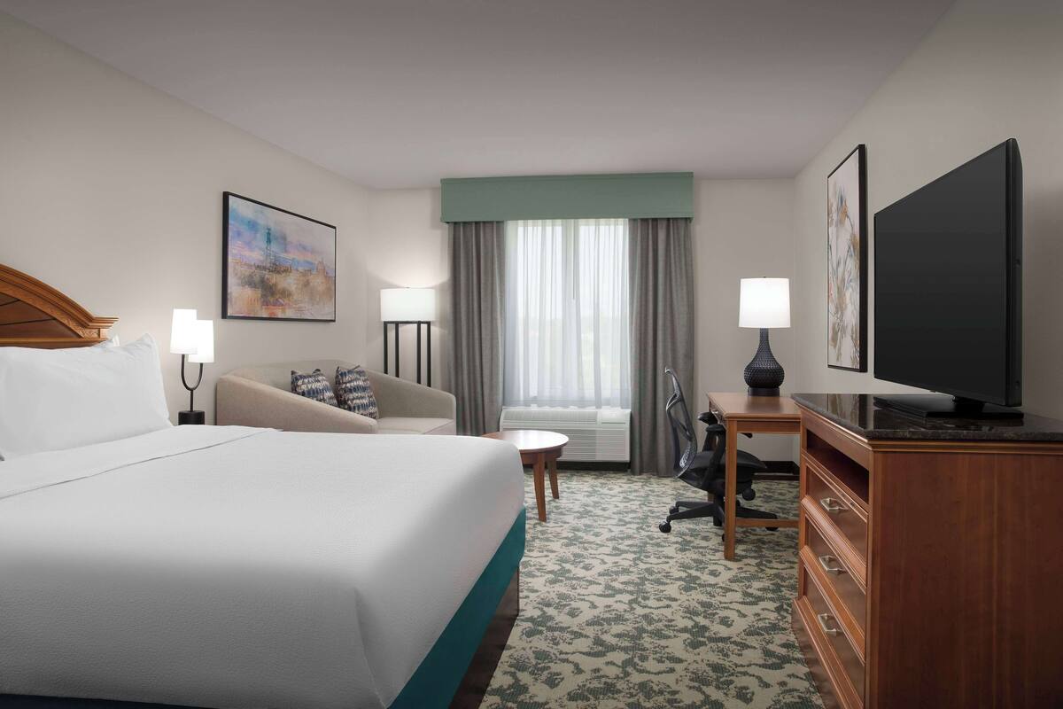 A hotel room with a bed, a desk, a chair, a television, and a window with curtains.