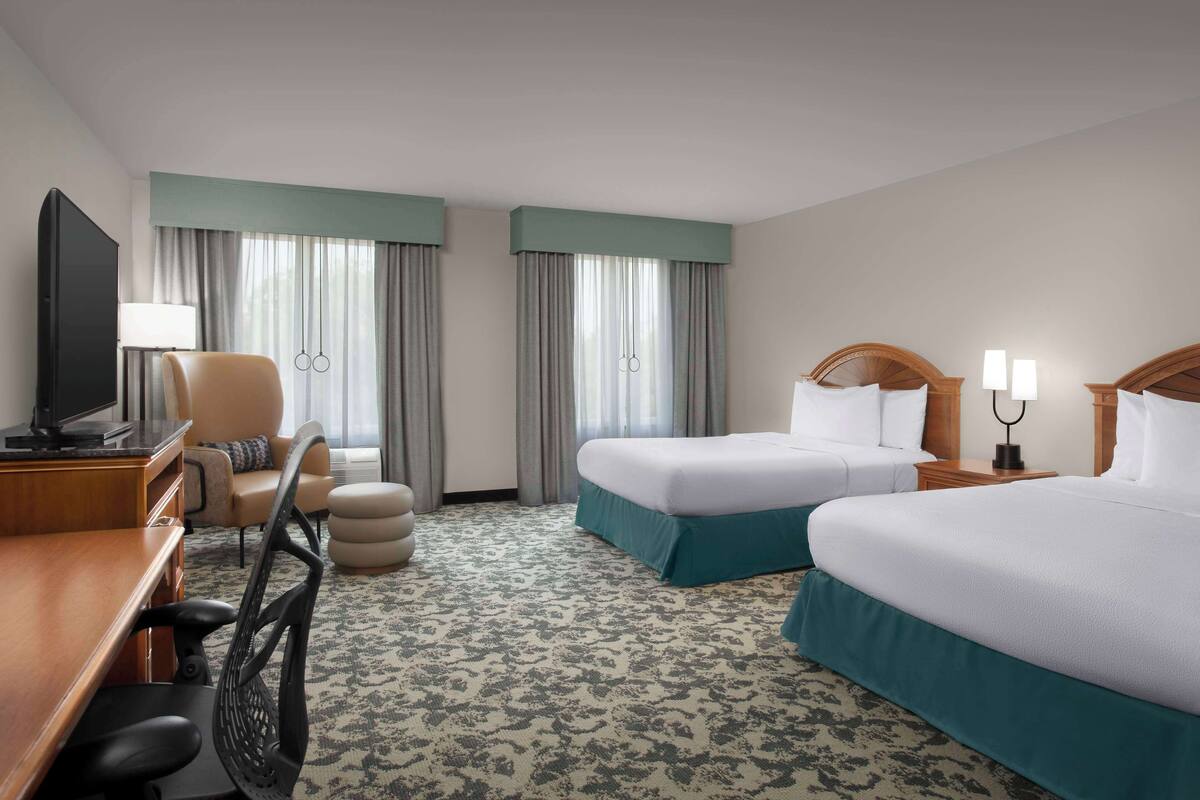 A hotel room with two beds, a desk with a TV, a chair, and a lamp.