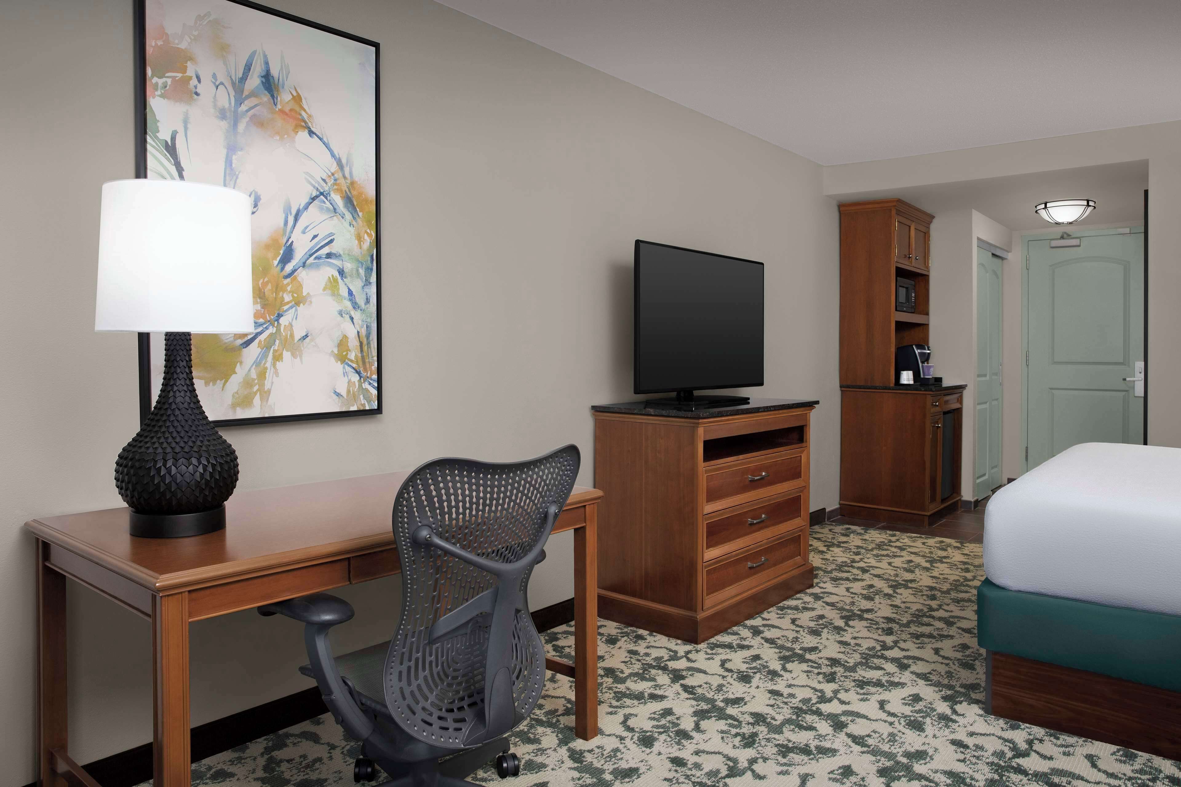 A hotel room with a desk, chair, television, wardrobe, and bed.