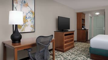 A hotel room with a desk, chair, television, wardrobe, and bed.