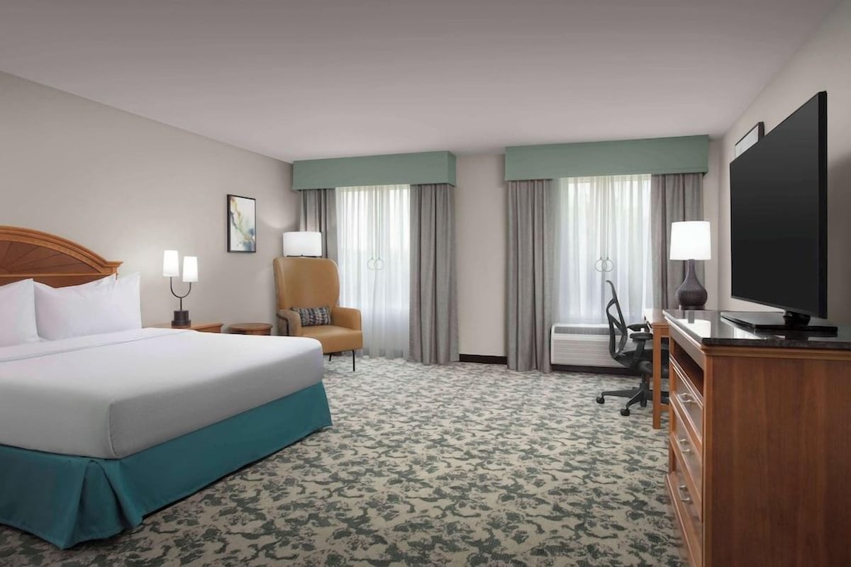 Una habitación de hotel con una cama grande, un escritorio con televisor, una silla y una lámpara de escritorio.