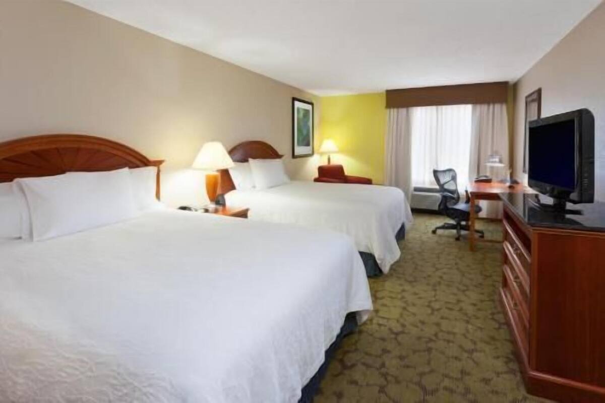 A hotel room with two beds, a desk, a television, and a chair.