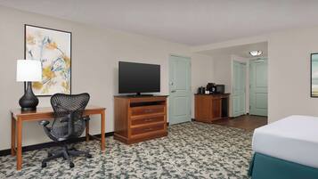 A hotel room with a bed, a desk with a chair, a television, a dresser, and a door.