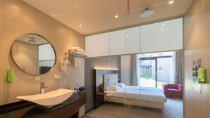 Une salle de bain d’hôtel moderne, dotée d’un grand lavabo, d’un miroir et d’un lit offrant une vue sur l’extérieur.